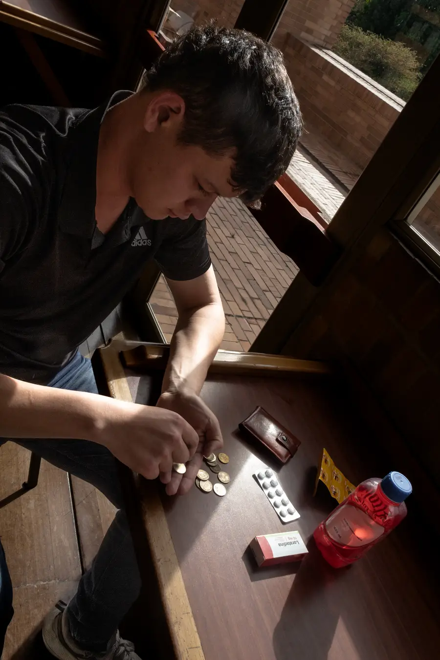 Persona contando monedas sobre una mesa junto a sus medicamentos