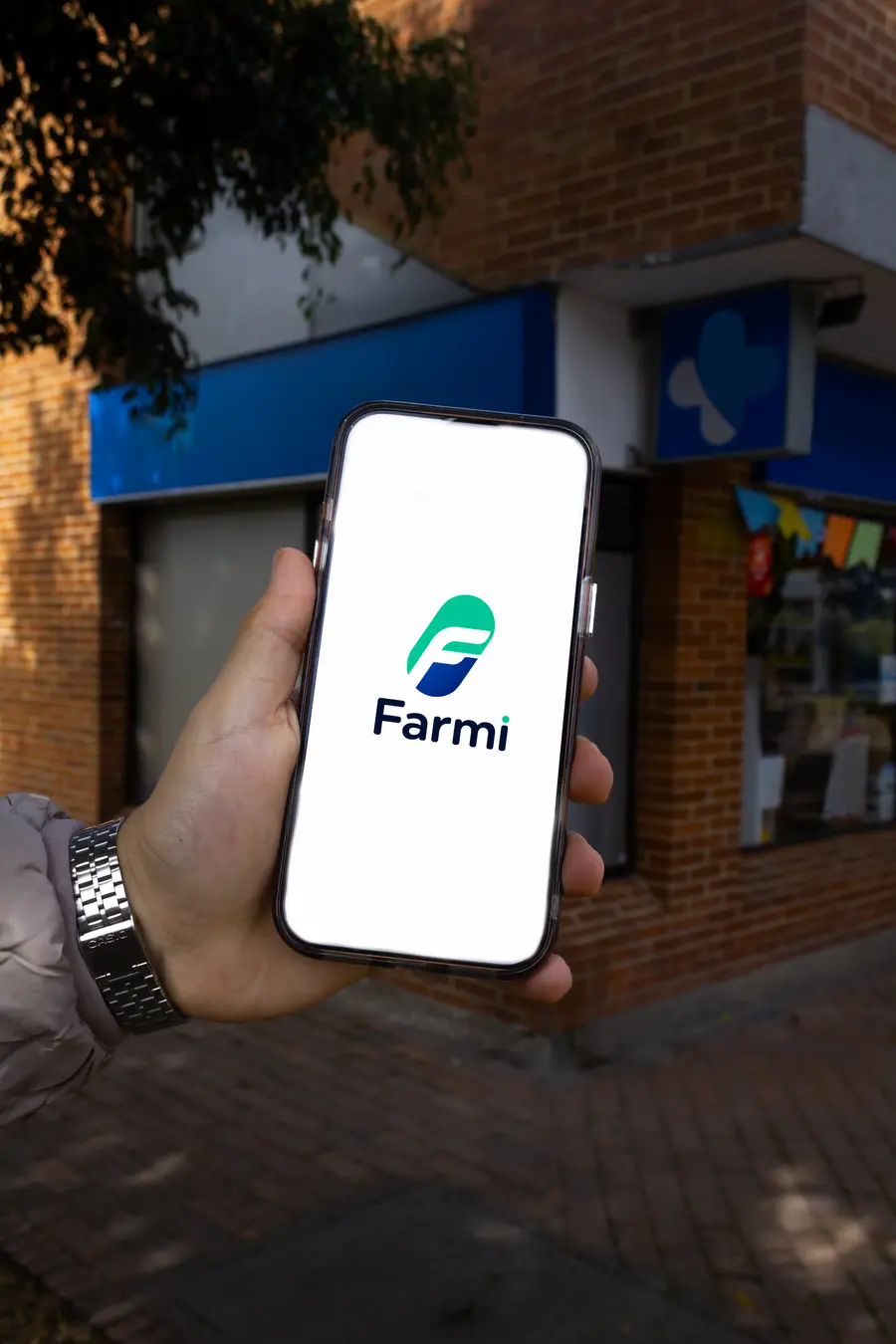 Celular mostrando el logo de Farmi frente a una droguería